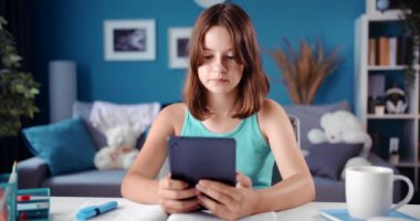 Genç kız ödevlerini yaparken tablette internette geziniyor.