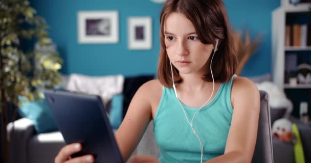 Keskittynyt tyttö kuulokkeet lukeminen sähköinen kirja kotona — kuvapankkivideo