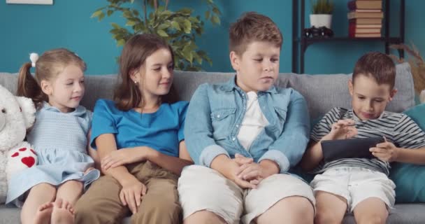 Glada två pojkar och två flickor som spelar på surfplatta hemma — Stockvideo