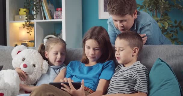 Happy children playing games on digital tablet on couch — Stock Video