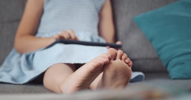 Nettes Mädchen mit Barfuß auf der Couch sitzend und mit Tablet — Stockvideo