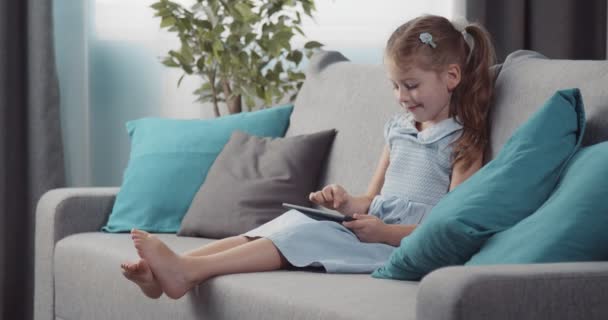 Menina sorridente sentada no sofá e usando tablet para desenhar — Vídeo de Stock
