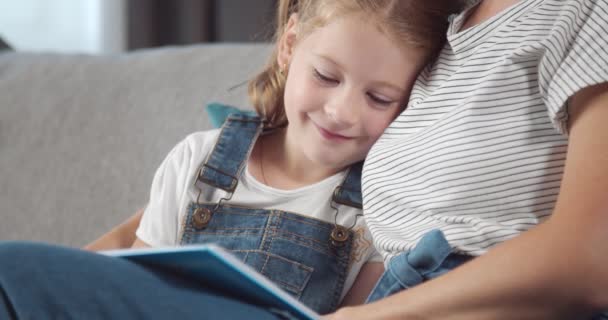 Happy girl hugging mother while reading book on grey couch — Stock Video