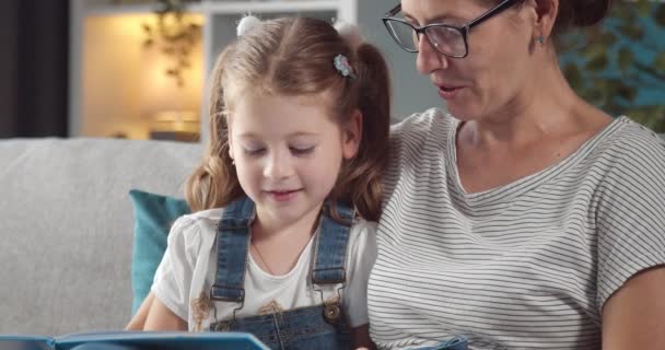 Mulher bonita livro de leitura com filha no sofá — Vídeo de Stock