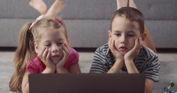 Ευτυχισμένα παιδιά ξαπλωμένα στο χαλί και βλέποντας κινούμενα σχέδια στο φορητό υπολογιστή — Αρχείο Βίντεο
