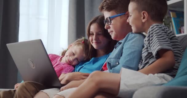 Fyra vänliga barn som kopplar av på soffan och använder laptop — Stockvideo