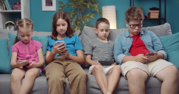 Empat anak menggunakan peralatan pribadi sambil bersantai di sofa — Stok Video