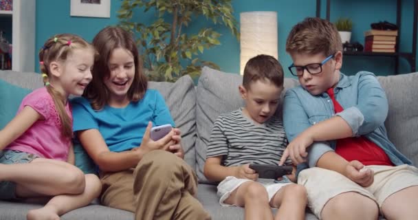 Fyra små barn använder smartphone och surfplatta på soffan — Stockvideo