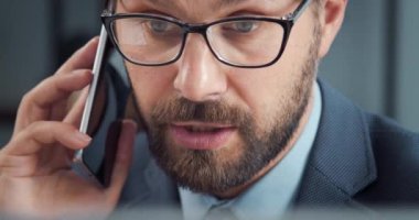 Bilgisayarda çalışan ve cep telefonuyla konuşan iş adamı.