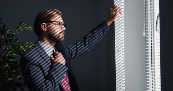 アイウェアを着た疲れた男とスーツはオフィスの窓の近くに立って — ストック動画