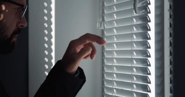 Vista lateral del hombre de negocios mirando a través de persianas de ventana — Vídeos de Stock