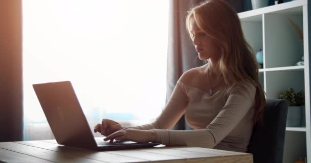 Приваблива жінка друкує на ноутбуці, сидячи за столом — стокове відео