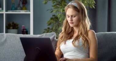 Kanepede dizüstü bilgisayarla gevşeyen sarı saçlı mutlu kız.