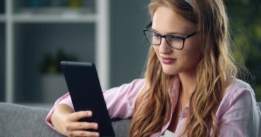 Gözlüklü hoş kız evde dinleniyor ve tablet kullanıyor.