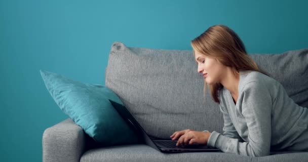 Widok z boku kobiety leżącej na kanapie i piszącej na laptopie — Wideo stockowe