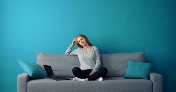 Zamyšlená dívka sedí na gauči s otevřeným notebookem — Stock video