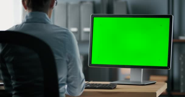 Vrouw zit op kantoor en kijkt naar groen computerscherm — Stockvideo