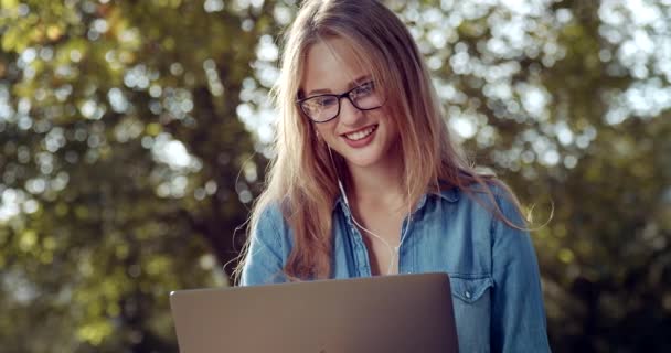 Loira sorrindo ter chamada de vídeo no laptop no parque — Vídeo de Stock