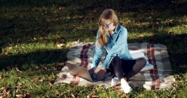 Parkta oturan ve dizüstü bilgisayarda yazan çekici kadın.