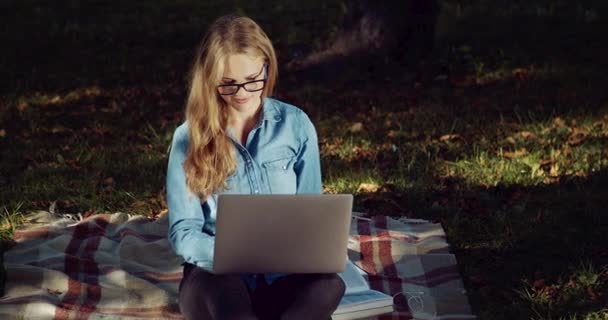 Loira sorridente usando laptop portátil para estudar no parque — Vídeo de Stock