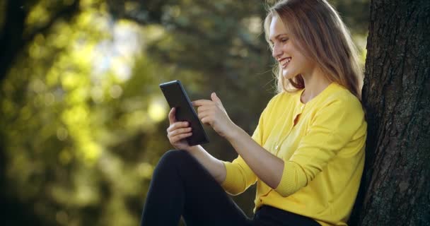 Весела жінка використовує цифровий планшет в літньому парку — стокове відео
