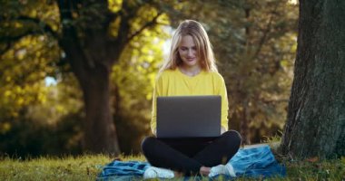 Gün batımında parkta dizüstü bilgisayarda yazan mutlu kadın.