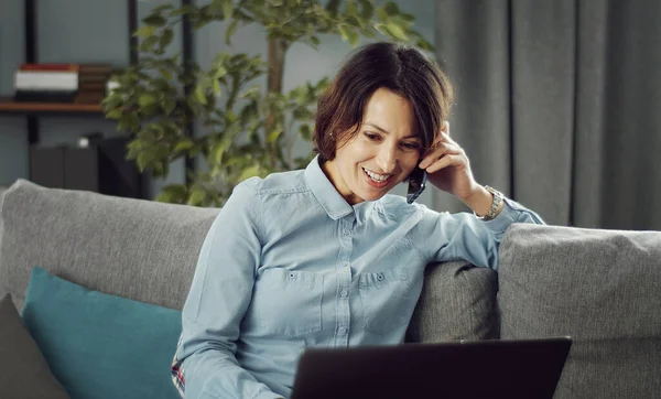 Mujer hablando teléfono usando el ordenador portátil — Foto de Stock