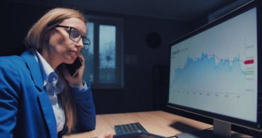 Finansal grafiklerle çalışan ve cep telefonuyla konuşan bir kadın