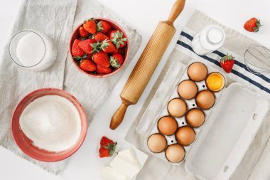 Hammaddelerini pişirme çilekli pasta ya da kek (yumurta, un, süt, şeker, çilek), beyaz arka plan üzerinde için en iyi görünümü, düz yatıyordu. Fırın arka plan. Çilekli pasta tarifi