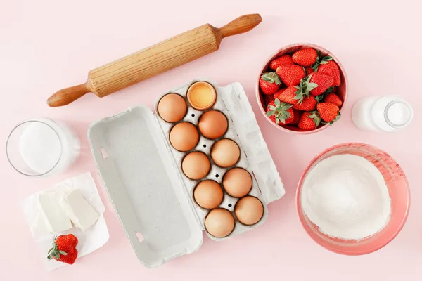 Çilekli pasta yemek için ham maddeler yat veya üstten görünüm pembe arka plan (yumurta, un, süt, şeker, çilek), kek. Fırın arka plan. Çilekli pasta tarifi