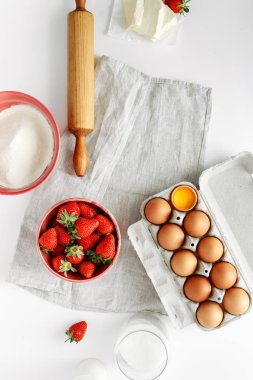 Çilekli pasta ya da kek metin veya nesne için boş alan ile beyaz masada yemek pişirmek için malzemeler. Düz yatıyordu, en iyi görünüm. Yumurta, un, süt, şeker, çilek, en iyi görünüm. Fırın arka plan. Çilekli pasta tarifini. Rustik tarzı