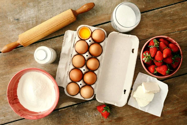 ingredients for cooking strawberry pie or cake on wooden background. Eggs, flour, milk, sugar, strawberry, top view. Bakery background. Recipe for strawberry pie. Rustic style