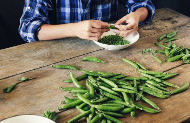 Temiz yeşil bezelye mutfakta ahşap masada oturan yakın çekim eller. Rustik tarzı. Ahşap masa üzerinde kase yeşil bezelye