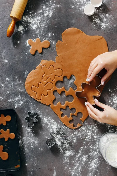 Top view christmas food concept. Woman is cooking gingerbread man cookies in Christmas on dark background, flat lay. Xmas dessert