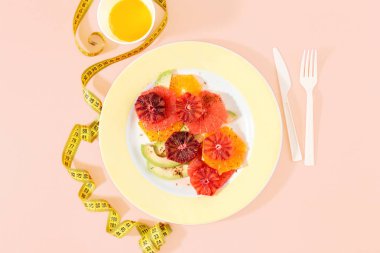 Portakal, greyfurt ve avokado ölçme bant ve portakal suyu ile pembe arka plan üzerinde sağlıklı diyet meyve salatası