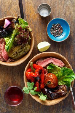 Ahşap masa, üstten görünüm tabaklarda ekmek ızgara biftek ve ızgara sebzeler servis