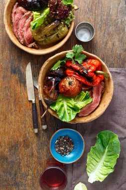 Ahşap masa, üstten görünüm tabaklarda ekmek ızgara biftek ve ızgara sebzeler servis