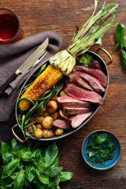 Dilim Dana biftek tavada kızarmış Mısır ve patates ile fesleğen sos ve bardak kırmızı şarap, üstten görünüm ile ahşap tabloda yeşil fasulye ile servis