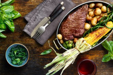 Dilim Dana biftek tavada kızarmış Mısır ve patates ile fesleğen sos ve bardak kırmızı şarap, üstten görünüm ile ahşap tabloda yeşil fasulye ile servis