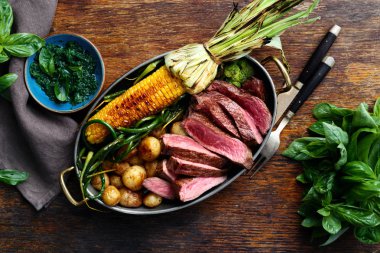 Dilim Dana biftek tavada kızarmış Mısır ve patates ile fesleğen sos ve bardak kırmızı şarap, üstten görünüm ile ahşap tabloda yeşil fasulye ile servis