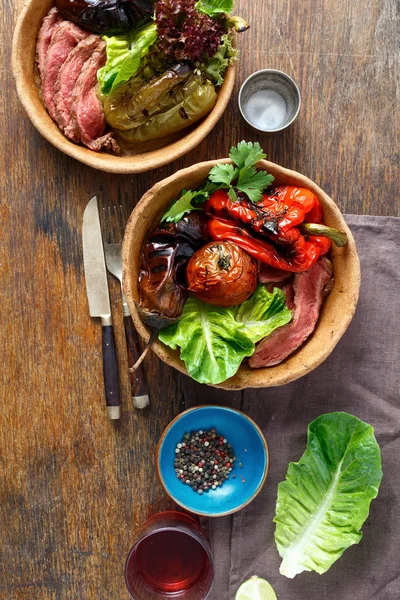 Ahşap masa, üstten görünüm tabaklarda ekmek ızgara biftek ve ızgara sebzeler servis