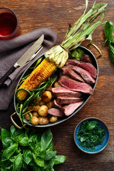 Dilim Dana biftek tavada kızarmış Mısır ve patates ile fesleğen sos ve bardak kırmızı şarap, üstten görünüm ile ahşap tabloda yeşil fasulye ile servis