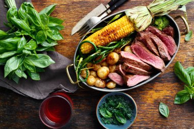 Dilim Dana biftek tavada kızarmış Mısır ve patates ile fesleğen sos ve bardak kırmızı şarap, üstten görünüm ile ahşap tabloda yeşil fasulye ile servis