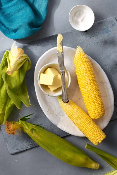 tereyağı ve tuz gri arka plan, üstten görünüm üzerinde ham tatlı Mısır ile plaka 