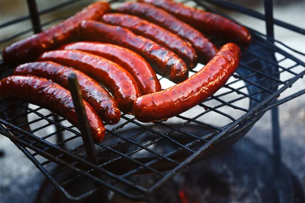 Grilled sausages on grill with flames and smoke
