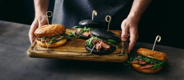 Adam ahşap tahta üzerinde ızgara sığır etli farklı burger tutar.