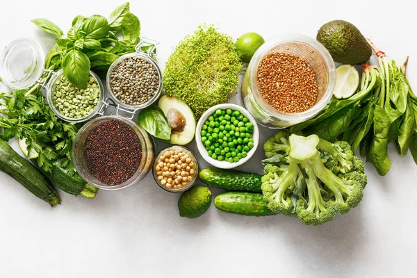 Set raw vegetables and grain products source of protein for vegetarians: cucumber, lucerne, zucchini, spinach, basil, green peas, avocado, broccoli, lime, buckwheat, green lentils, chickpea and quinoa on white concrete background, top view