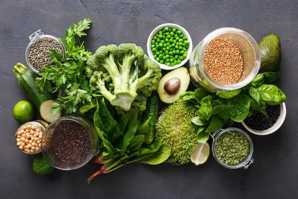 Set raw vegetables and grain products source of protein for vegetarians: cucumber, lucerne, zucchini, spinach, basil, green peas, avocado, broccoli, lime, buckwheat, green lentils, chickpea and quinoa on black background, top view