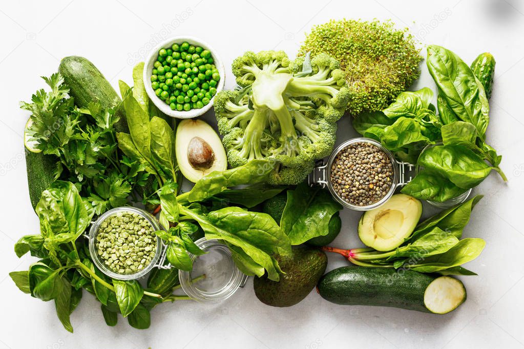 Set raw healthy food clean eating vegetables and grain products source of protein for vegetarians: cucumber, lucerne, zucchini, spinach, basil, green peas, avocado, broccoli, lime and green lentils on white concrete background, top view