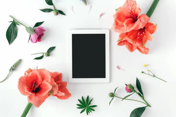 Düz yatıyordu beyaz tabletiyle boş masaüstü ekran ve çiçekler peonies, nergis zambağı beyaz arka planda, üstten görünüm